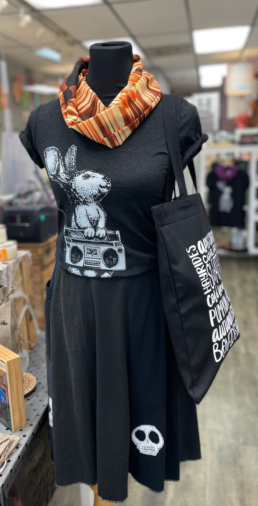Image shows a mannequin dressed in an orange scarf, a charcoal grey t-shirt with a bunny holding a boombox printed on it, and skirt with appliqued skulls on the hem.