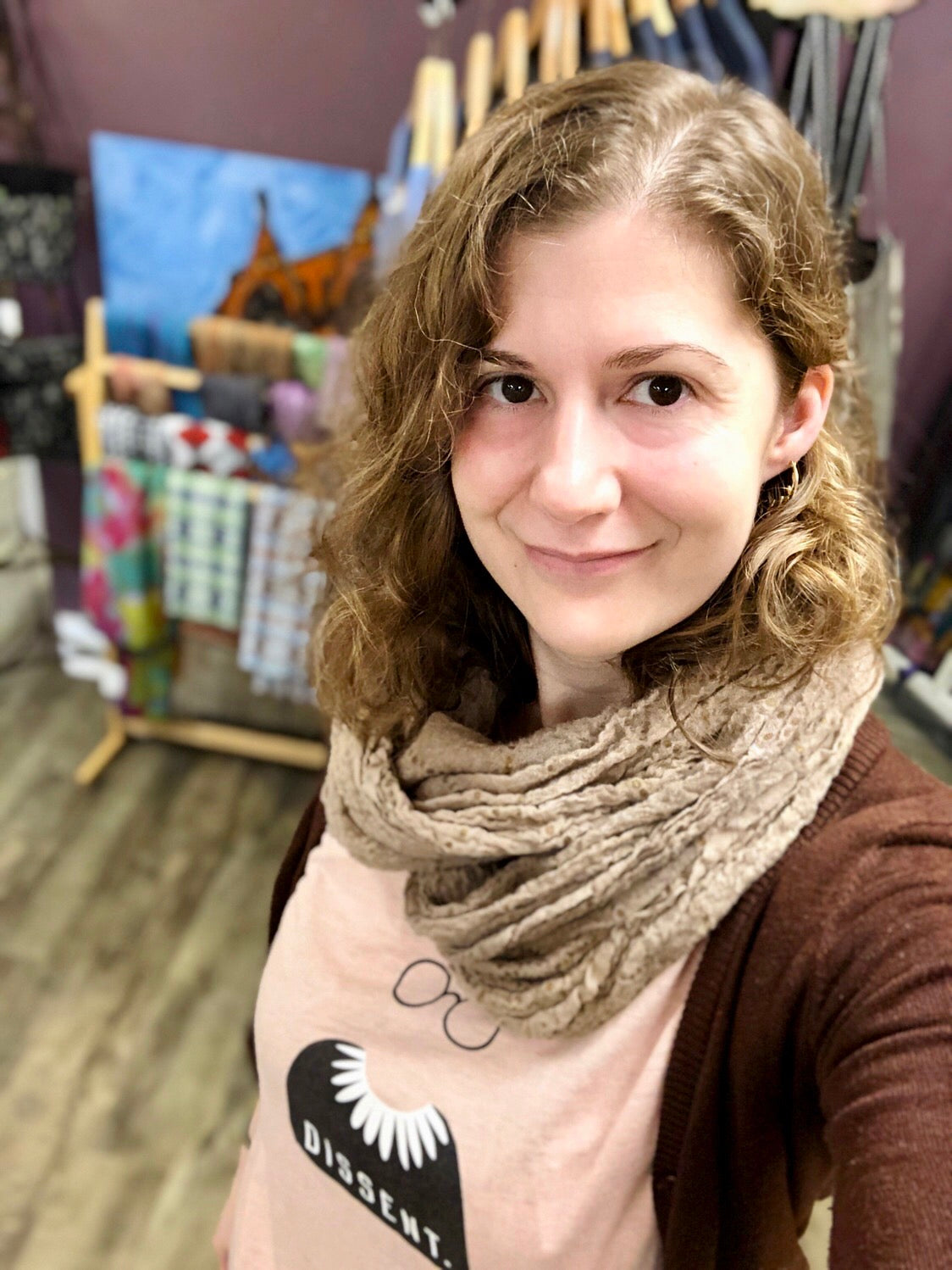 Image is of shop owner, Sumner. Sumner has brown eyes and honey-colored curly hair. She wears a pink t-shirt and a brown cardigan.